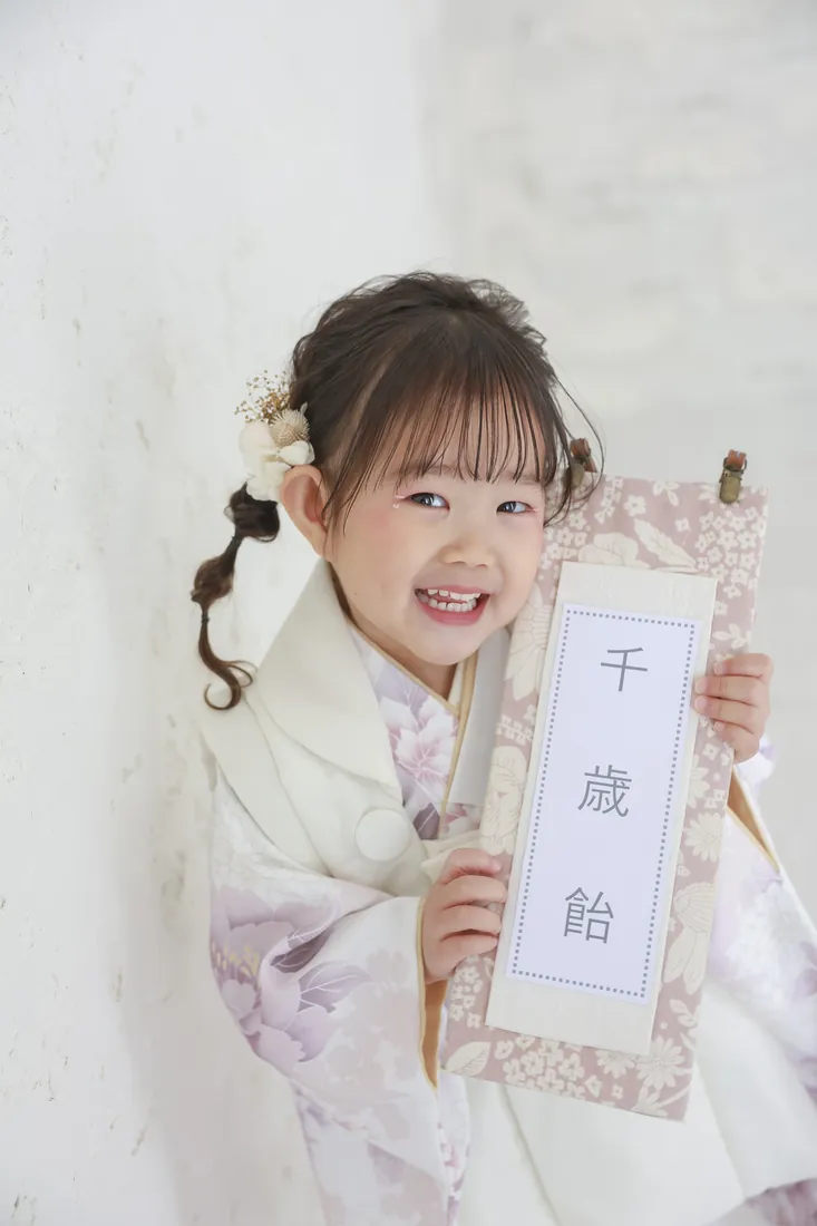 被布を着て千歳飴を持ち、笑顔を見せる3歳の七五三の女の子